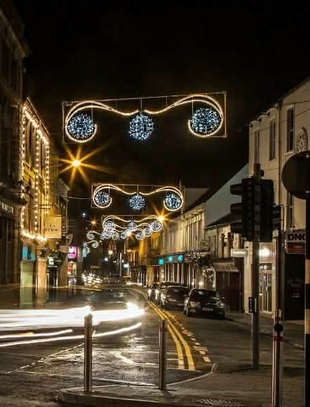 Street scene with festive lights hanging above a city street at night.